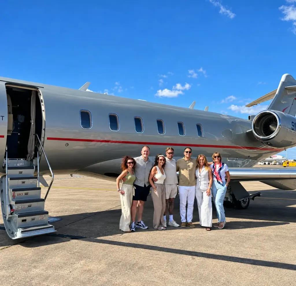 A group of travellers standing beside a private jet on a sunny airfield